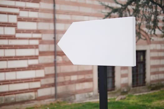 Blank sign points towards an unknown direction near a red brick building.