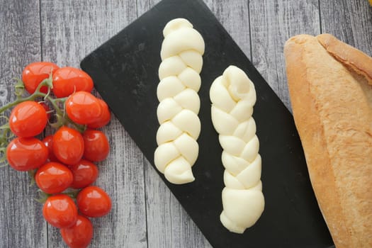 Braided cheese and fresh cherry tomatoes are arranged on a black board.