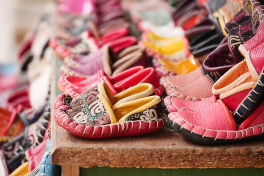 Numerous colorful handmade shoes are arranged on a wooden table for sale.