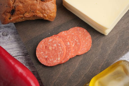 Salami slices are arranged on a wooden board with cheese and bread nearby.