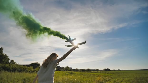 A young girl with a toy airplane smokes colorful smoke on a summer evening