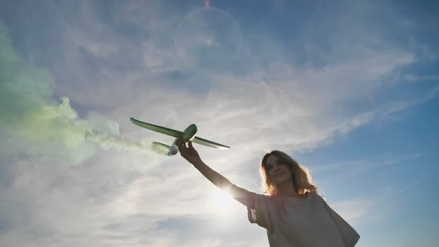A young girl with a toy airplane smokes colorful smoke on a summer evening