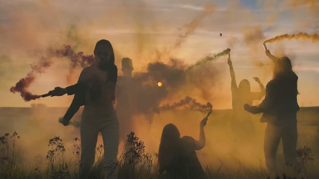 Happy friends girls waving colorful smoke at sunset