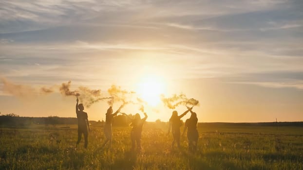 Happy friends waving colorful smoke at sunset
