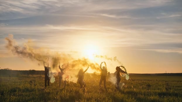 Happy friends waving colorful smoke at sunset
