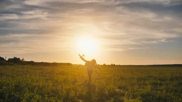 A young girl runs with a toy airplane against the sunset sky