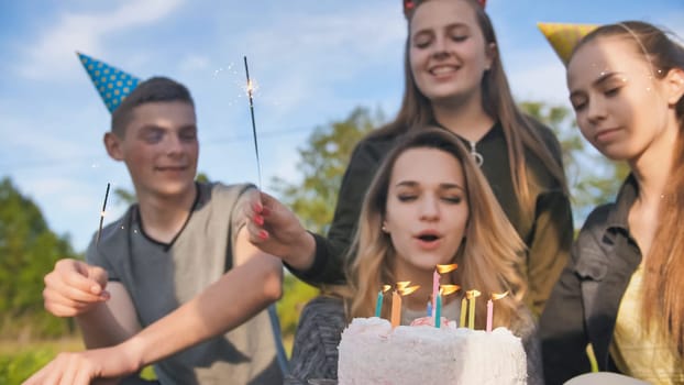 Happy friends celebrate their girlfriend's birthday. The birthday girl blows out the candles