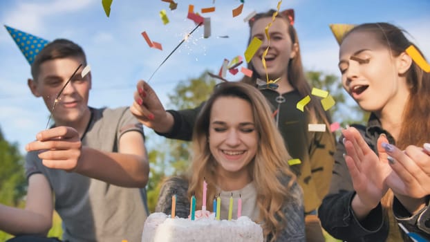 Happy friends celebrate their girlfriend's birthday. The birthday girl blows out the candles