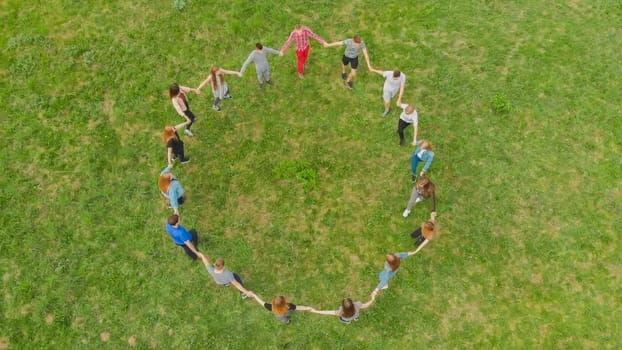 Friends in a circle holding hands make a round dance in the field