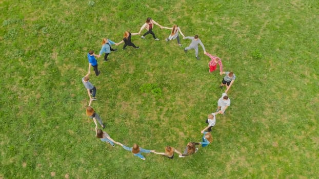 Friends in a circle holding hands make a round dance in the field
