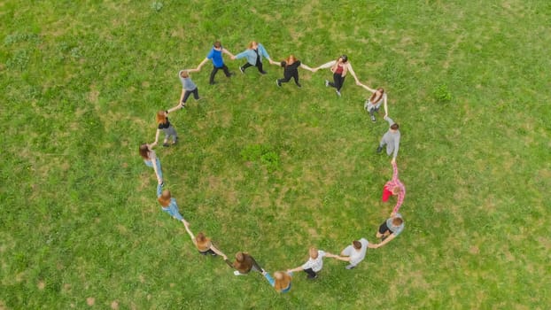Friends in a circle holding hands make a round dance in the field