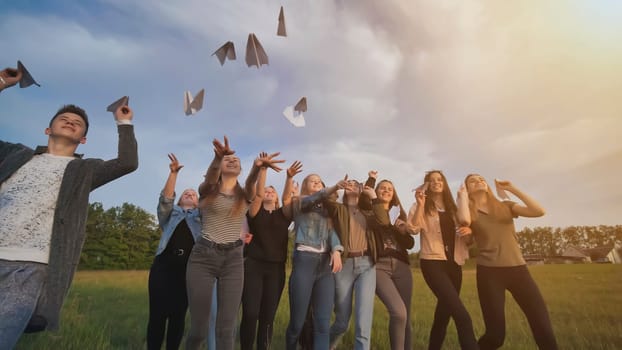 Happy friends launch paper airplanes at sunset