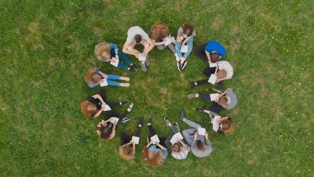 A group of students are sitting in a circle and books on the grass