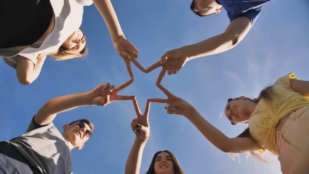 Friends make a star shape from their hands against a blue sky.