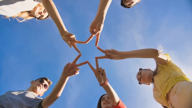 Friends make a star shape from their hands against a blue sky.