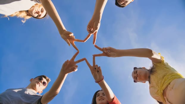 Friends make a star shape from their hands against a blue sky.
