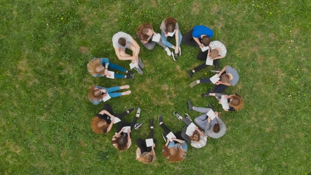 A group of students are sitting in a circle and books on the grass