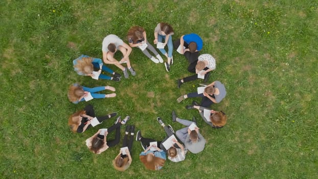 A group of students are sitting in a circle and books on the grass