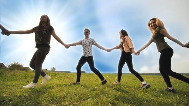 A group of young people lead a round dance holding hands on a summer day. Unity concept