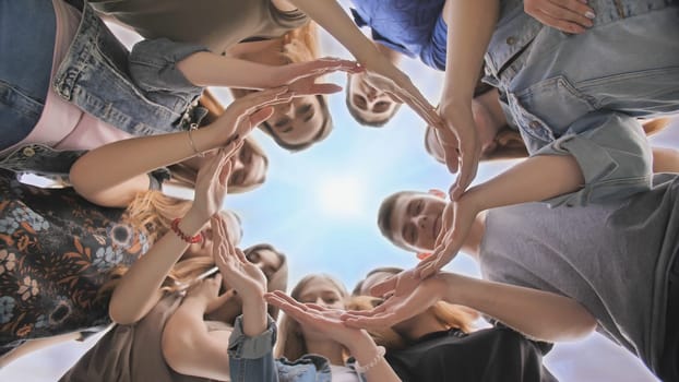Young people putting their hands in circle on sky background. Unity concept