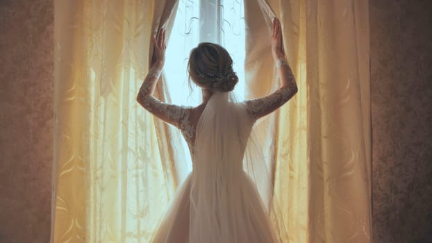 The bride opens the curtains on the window at home