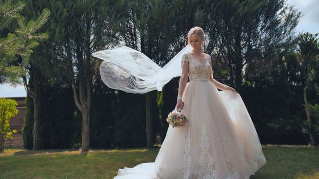 A young bride is standing in a park and her veil is slowly falling her veil is slowly falling.