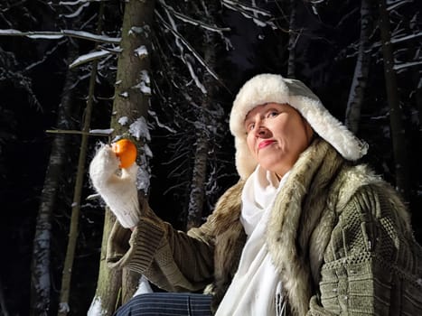 A funny middle-aged woman takes a whimsical stroll in the snowy woods at night, playfully holding a balalaika and orange.
