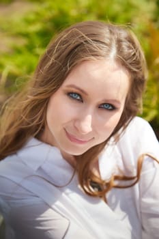 A young woman with blue eyes and brown hair enjoys a sunny day outdoors in a vibrant green environment.