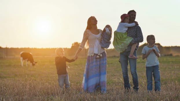 A large family goes on the field in the village during sunset