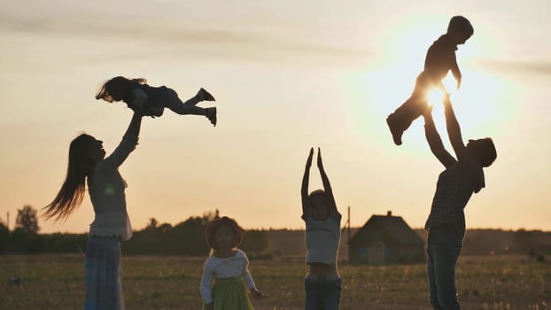 Happy parents tossing their children up on a sunset background. The concept of a happy large family.