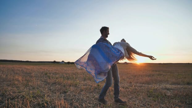 A guy is circling his girlfriend in his arms on a sunset background