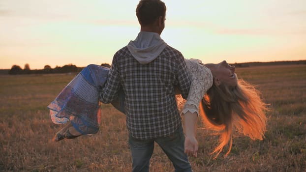 A guy is circling his girlfriend in his arms on a sunset background