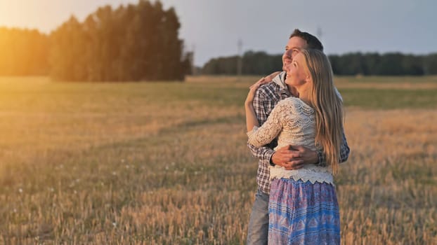 Young husband and wife cuddle at sunset and look towards the sun.