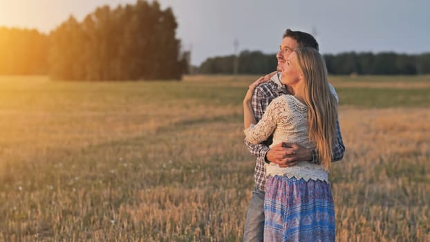 Young husband and wife cuddle at sunset and look towards the sun.