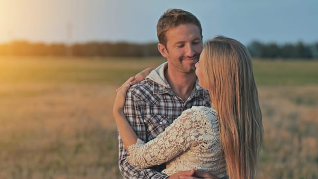 Young husband and wife cuddle at sunset and look towards the sun.