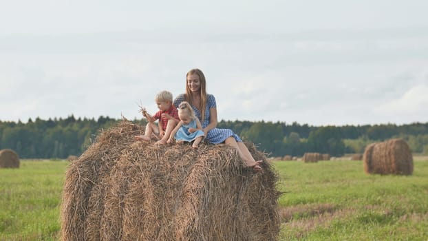 A mother with two children sits on a sheaf of straw in a field