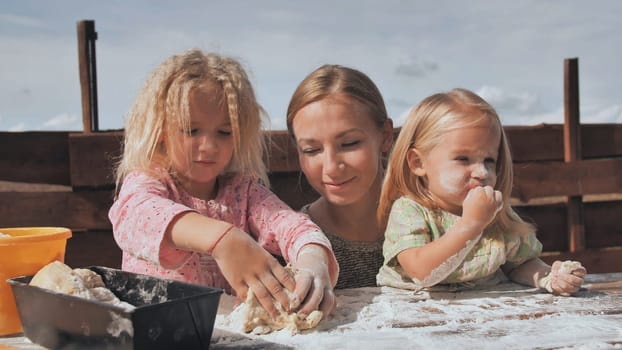 Two daughters knead the dough with their hands next to their mother. Homemade bread baking
