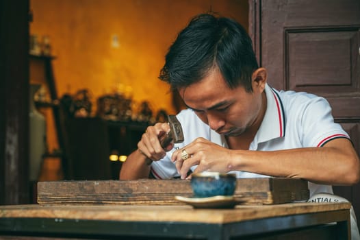 Vietnamese Asian man artisan craftsman works in a jewelry workshop on street in Hoi An city in Vietnam in Asia. Hoi An, Vietnam - December 2, 2024