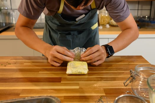 Close up of hands wrapping freshly made compound butter on a wooden countertop.