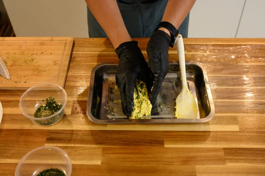 Overhead view of man mixing compound butter with fresh herbs and garlic on kitchen counter.