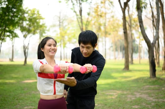 Active man and woman exercising with dumbbells together in a green park.