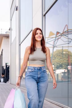 young adult woman in casual clothes walking down a sidewalk near of a mall carrying shopping bags, concept of youth and urban lifestyle, copyspace for text