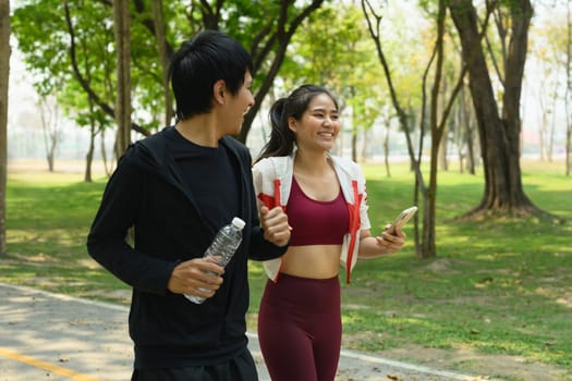Happy man and woman walking through a green park after workout session.