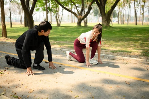 Active young couple crouch in start line pose preparing to sprint in a park.