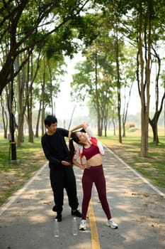 Athletic couple stretching together before a run on a sunlit park path.