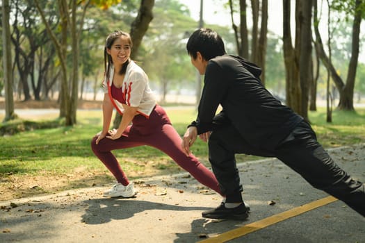 Athletic couple stretching together before a run on a sunlit park path.
