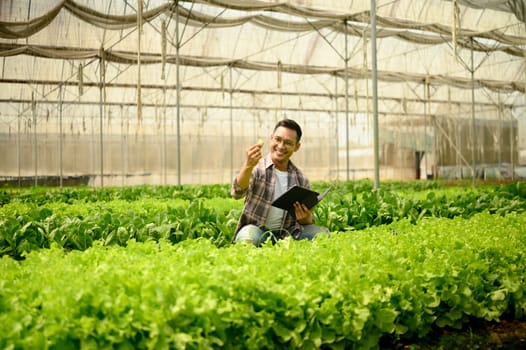 Smiling farmer using digital tablet while inspecting crops in a greenhouse. Concept of modern agriculture.