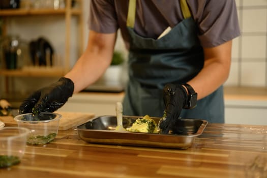 Man wearing black gloves mixing compound butter with fresh herbs and garlic on kitchen counter.
