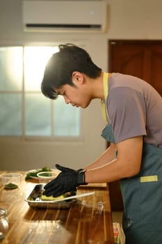 Focused man mixing compound butter with fresh herbs and garlic on kitchen counter.