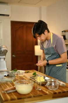 Young man wearing an apron preparing fresh herbs for compound butter.